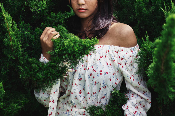 Asian beautiful woman Face and beautiful skin with freckles, wearing a white dress, the background is a dark green Platycladus orientalis leaf Under the concept of fashion And natural beauty products - Photo, Image