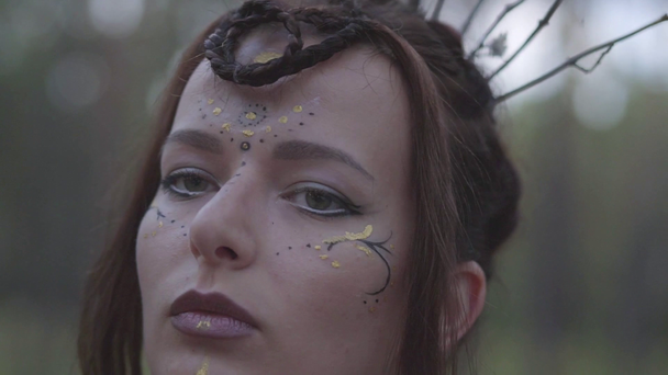 Portrait of an attractive dryad or forest fairy with a wreath of branches on the head and painted the third eye on the forehead dancing under the trees. Ancient ritual of forest creature. Slow motion. - Footage, Video