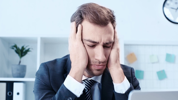 Unzufriedener Geschäftsmann bedeckt Kopf mit Händen, während er am Arbeitsplatz im Büro sitzt - Filmmaterial, Video