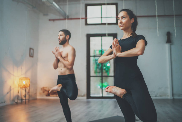 Concepto de clase de ejercicio de práctica de yoga. Mujer joven y hombre practicando yoga en interiores. Dos deportistas haciendo ejercicios
. - Foto, imagen