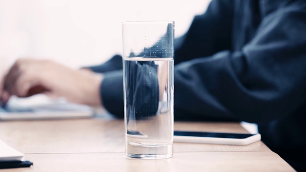 vue partielle de l'homme d'affaires boire de l'eau du verre tout en utilisant un ordinateur portable sur le lieu de travail
 - Séquence, vidéo