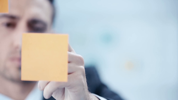 thoughtful businessman writing at sticky notes fixed on transparent flipchart in office - Séquence, vidéo