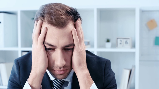 Unzufriedener Geschäftsmann bedeckt Kopf mit Händen und gestikuliert, während er am Arbeitsplatz im Büro sitzt - Filmmaterial, Video