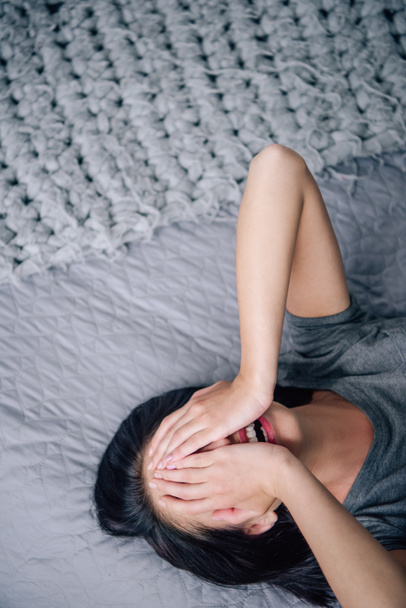 depressieve vrouw bedekt gezicht en huilen terwijl liggend op bed thuis - Foto, afbeelding