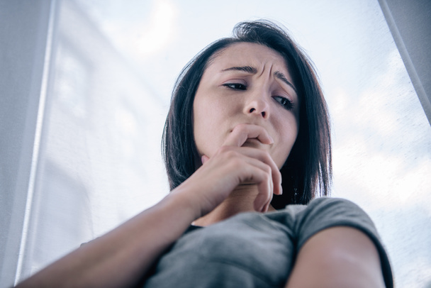 низкий угол зрения на красивую депрессивную женщину, покрывающую рот дома
 - Фото, изображение