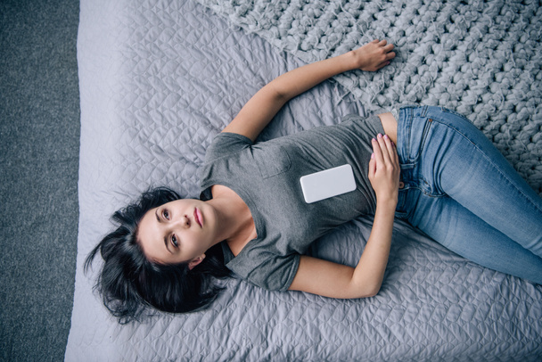 top view of lonely woman on bed with smartphone in bedroom - Photo, Image