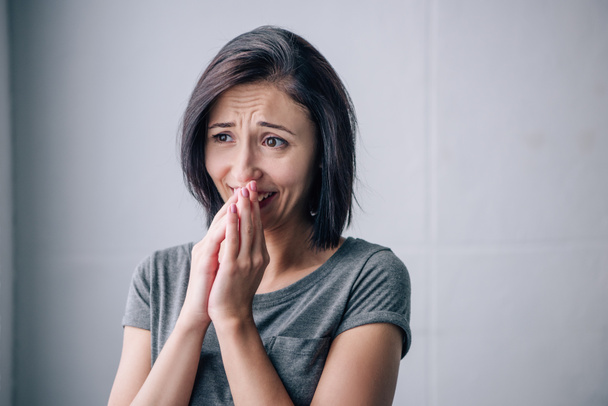 sad brunette woman covering mouth and crying at home - Foto, afbeelding