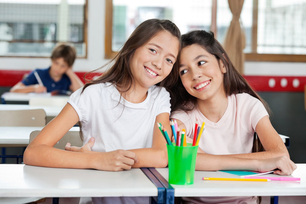 Schoolgirl Sitting With Female Friend At Desk In Classroom - Foto, Imagen