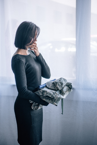 depressieve vrouw die militaire kleding in huis houdt - Foto, afbeelding