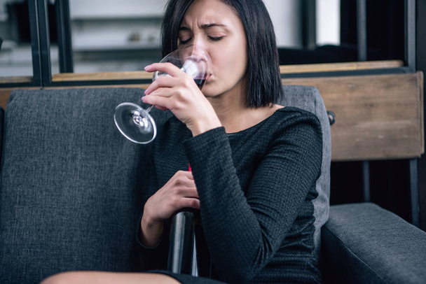depressieve vrouw zittend op de Bank en het drinken van wijn thuis - Foto, afbeelding