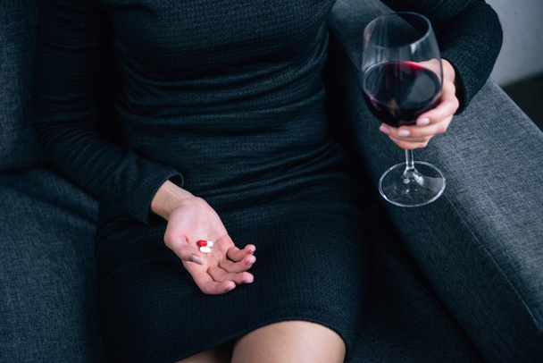 vista parcial de la mujer con copa de vino y pastillas en casa
 - Foto, Imagen