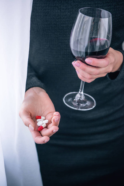 частичный вид подавленной женщины с бокалом вина и таблетками дома
 - Фото, изображение