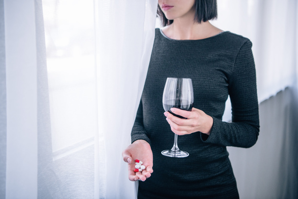 Ausgeschnittene Ansicht einer depressiven Frau mit Weinglas und Pillen zu Hause - Foto, Bild