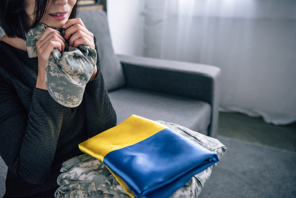 自宅で軍服とウクライナの旗を持つ動揺した女性のトリミングされたビュー - 写真・画像