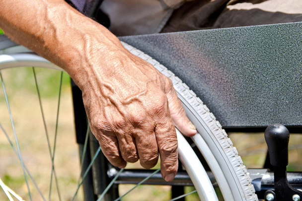 Ein behinderter Mann sitzt im Rollstuhl, hält die Hände an den Händen. - Foto, Bild