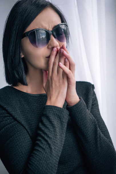 депрессивная одинокая женщина в солнечных очках, покрывающих рот и скорбящих дома
 - Фото, изображение