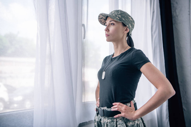 красива жінка з рукою на стегні в військовій формі вдома з копіювальним простором
 - Фото, зображення