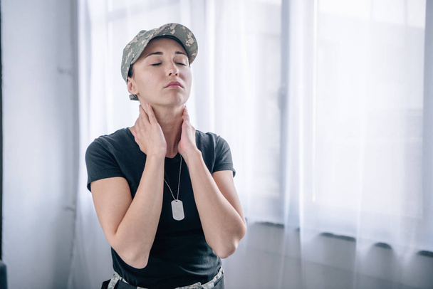 schöne Frau in Militäruniform, die zu Hause den Hals berührt - Foto, Bild