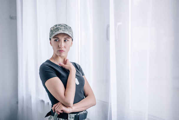 Depressive Frau in Militäruniform zu Hause und schaut weg  - Foto, Bild