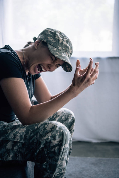 mujer deprimida en uniforme militar sentada en el sofá y gritando en casa
 - Foto, Imagen