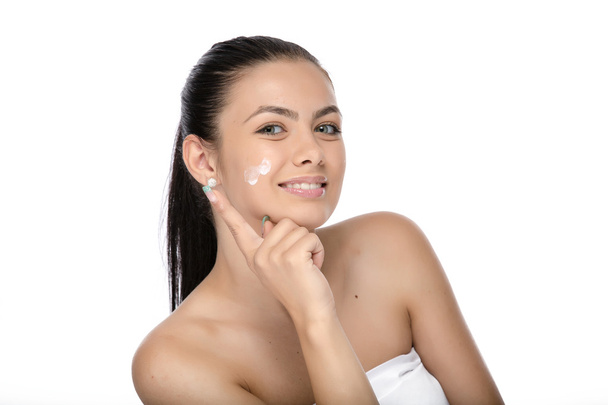 Bellissimo viso di giovane donna con crema cosmetica su una guancia. Ritratto da primo piano isolato su bianco
. - Foto, immagini