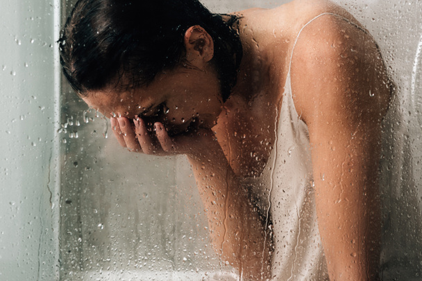 lonely depressed woman crying in shower through glass with water drops - Foto, afbeelding