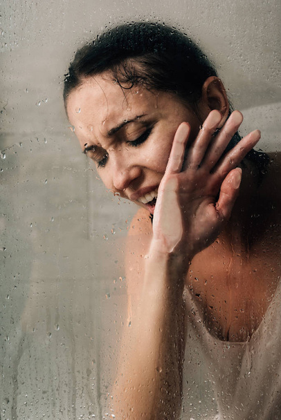 mujer deprimida solitaria llorando en la ducha a través de vidrio con gotas de agua
 - Foto, imagen