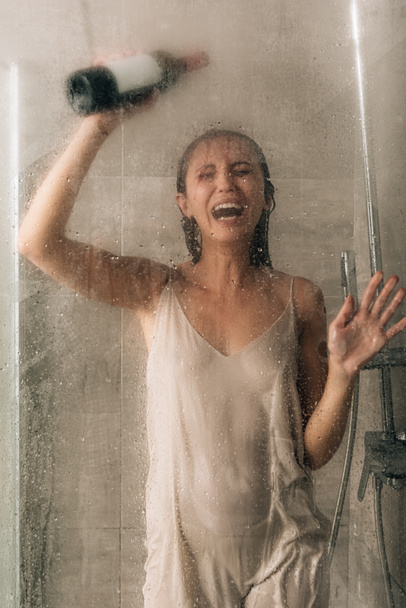 mujer deprimida solitaria en la ducha sosteniendo botella de vino y llorando en casa
 - Foto, imagen