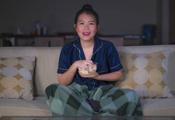 Mladá krásná šťastná a uvolněná asijská žena v obývacím pokoji, kde sedí útulně na pohovce a dívá se na televizní seriál nebo romantický komediální film s úsměvem sladkého - Fotografie, Obrázek