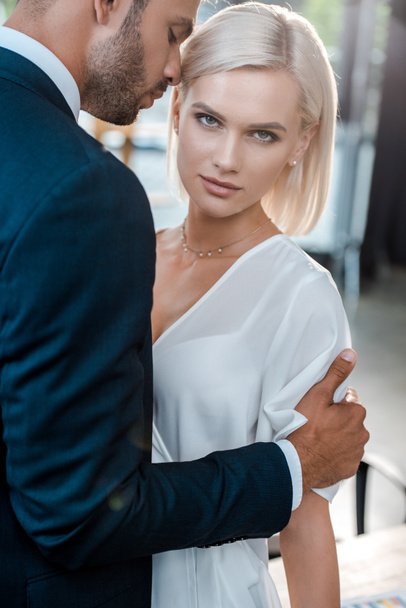 handsome bearded man hugging attractive blonde woman looking at camera - Zdjęcie, obraz