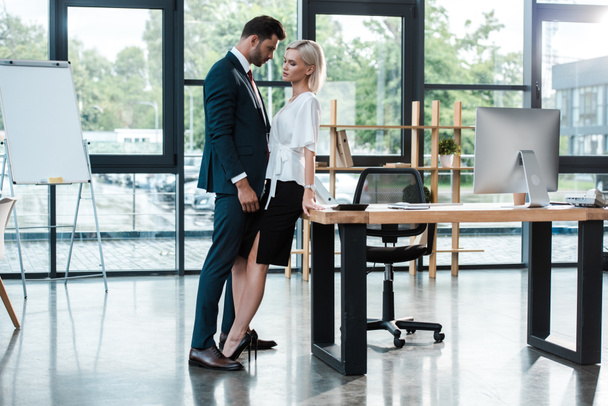 όμορφος επιχειρηματίας αγγίζοντας ελκυστική νεαρή γυναίκα, ενώ φλερτ στο γραφείο  - Φωτογραφία, εικόνα