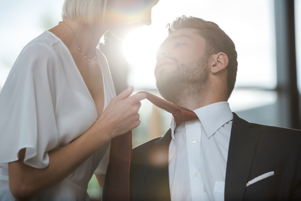 cropped view of passionate woman touching tie of handsome man while flirting in office  - 写真・画像