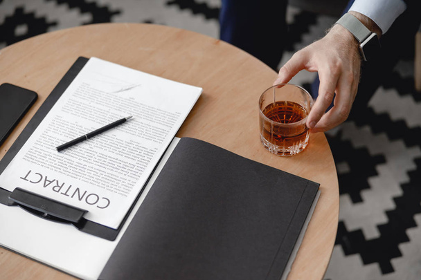 Hand of man putting glass of whisky near the contract - 写真・画像