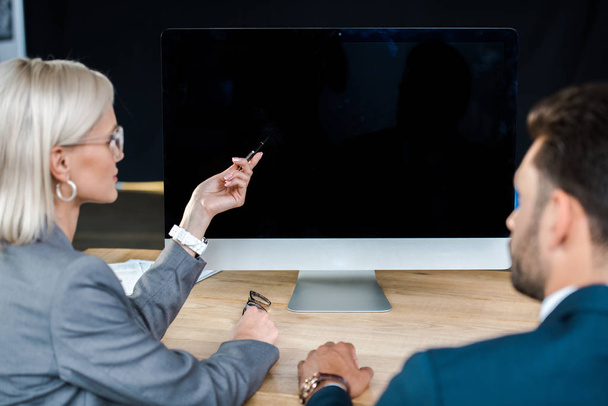 selective focus of computer monitor with blank screen near businessman and businesswoman  - Foto, Imagen
