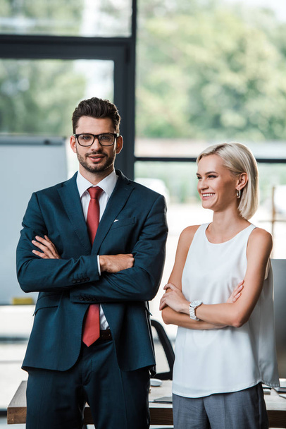 cheerful businessman in glasses and attractive businesswoman standing with crossed arms  - Foto, imagen