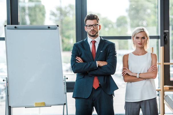 handsome businessman in glasses and beautiful blonde woman standing with crossed arms in office  - Photo, image