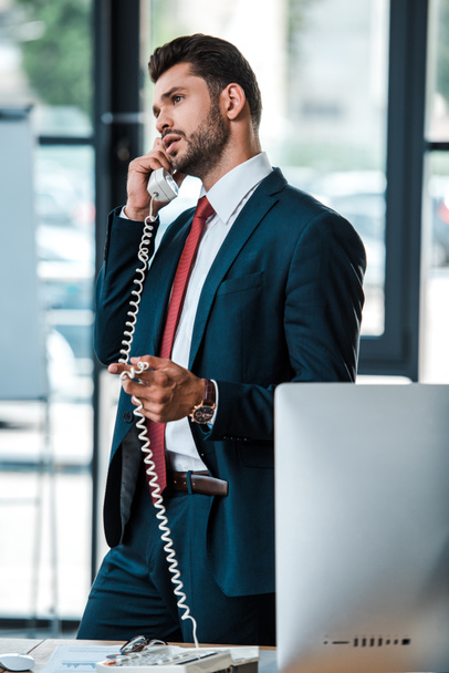 selective focus of handsome bearded businessman talking on retro phone in office  - Photo, Image