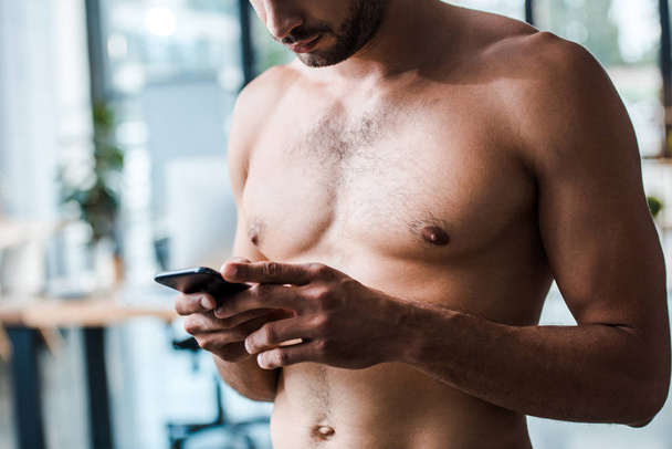 vista recortada del hombre sin camisa y musculoso utilizando el teléfono inteligente
  - Foto, Imagen