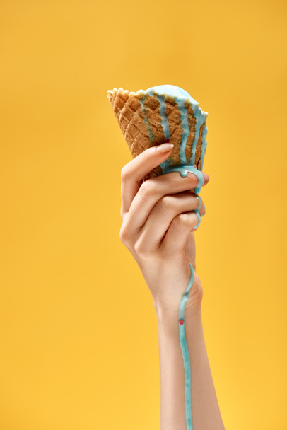 cropped view of woman holding delicious melted blue ice cream in crispy waffle cone isolated on yellow - Фото, изображение
