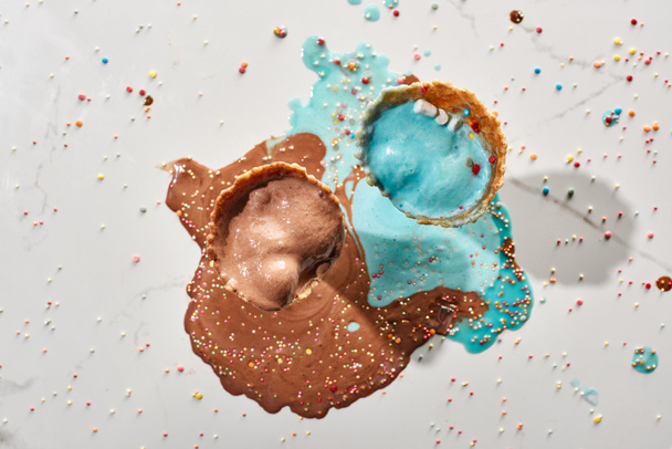 top view of delicious melted chocolate and blue ice cream in waffle cones on marble grey background with sprinkles - Photo, Image