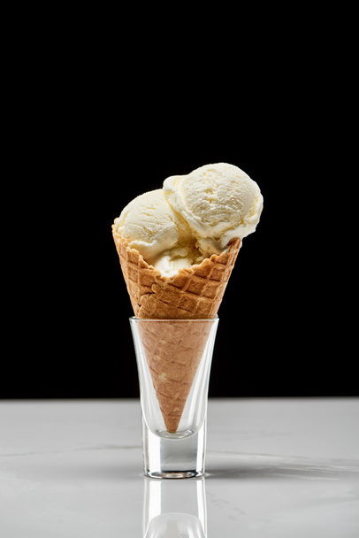 νόστιμο παγωτό βανίλια σε τραγανή χωνάκι από βάφλα απομονωμένο σε μαύρο  - Φωτογραφία, εικόνα