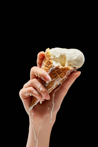 partial view of woman holding melting delicious vanilla ice cream in crispy waffle cone isolated on black  - Photo, Image