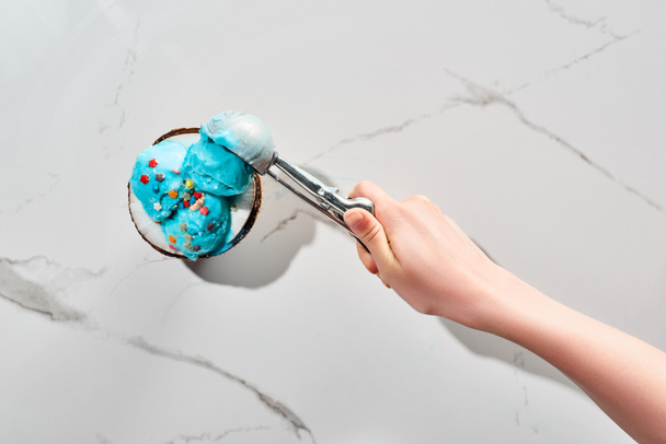 vista cortada de mulher tomando delicioso sorvete azul com polvilhas na metade de coco com colher no fundo cinza mármore
 - Foto, Imagem