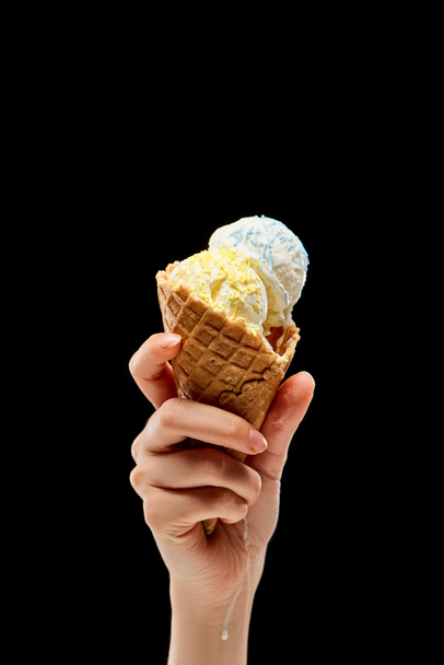 黒で隔離されたサクサクワッフルコーンに振りかけるおいしいバニラアイスクリームを持つ女性のトリミングビュー  - 写真・画像