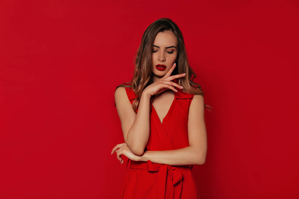 Romantic stylish woman in evening red dress posing over isolated red background while has a photoshoot - Photo, Image