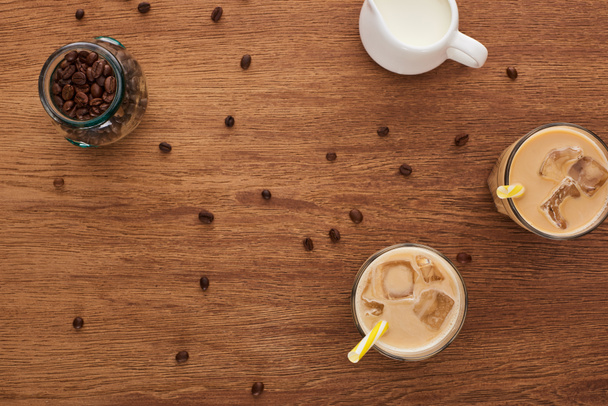 top view of ice coffee in glasses, milk and coffee grains on wooden table - Photo, Image