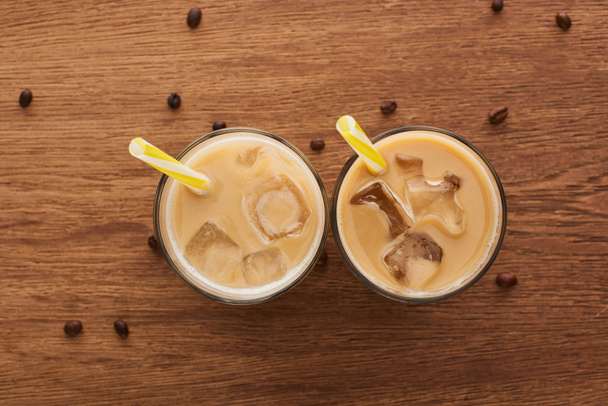 top view of fresh ice coffee in glasses with straws and coffee grains on wooden table - Photo, Image