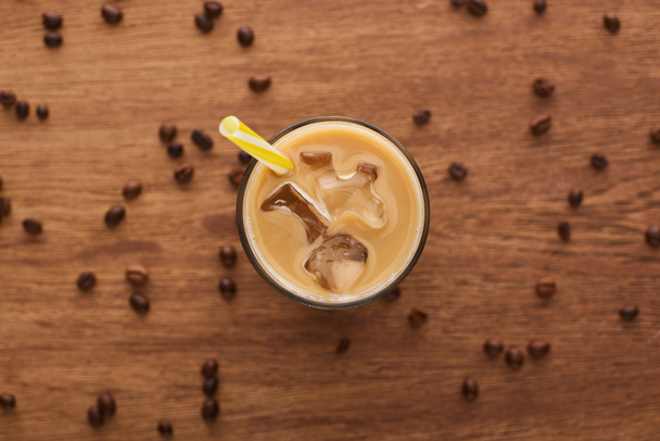 selective focus of ice coffee with straw in glass and coffee grains on wooden table - Photo, Image