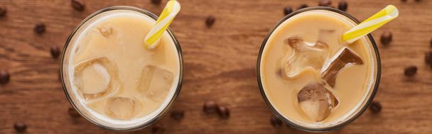 selective focus of ice coffee with straws in glasses and coffee grains on wooden table, panoramic shot - Photo, Image