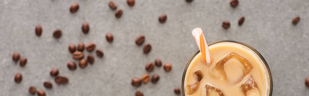 selective focus of ice coffee in glass with straw and coffee grains on grey background, panoramic shot - Valokuva, kuva